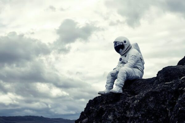 Astronaut sitzt nachdenklich auf Felsen