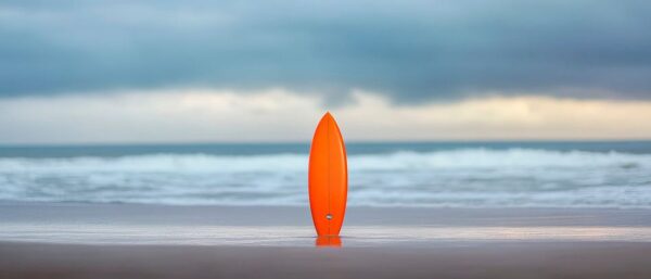 Orange Surfbrett am Strand bei Sonnenuntergang