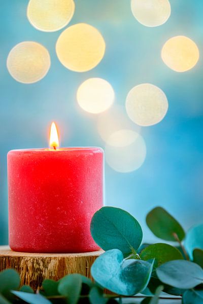 Rote Kerze mit Eukalyptus und Lichtbokeh